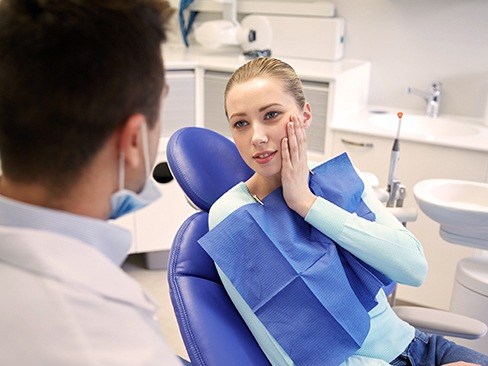 Woman in dental chair holding cheek during emergency dentistry visit