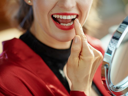 Woman smiling pointing at dental crown in Dallas