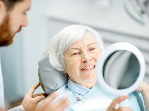 An older woman with dentures looking at her smile in the mirror