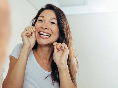 Woman flossing to prevent dental emergencies in Dallas