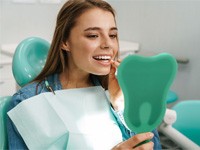 Female dental patient checking her teeth in a handheld mirror