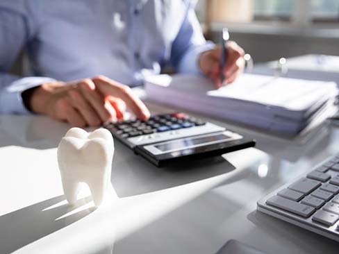 person typing on a calculator that is next to an artificial tooth