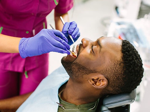 Man smiling while dental assistant examines patient's teeth