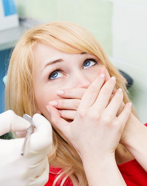 Woman in need of sedation dentistry in dental chair covering her mouth