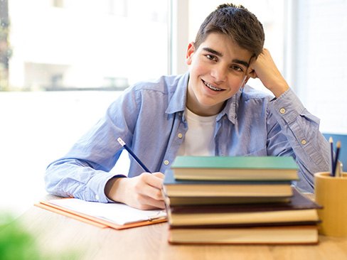 a teen with braces smiling and studying at a table