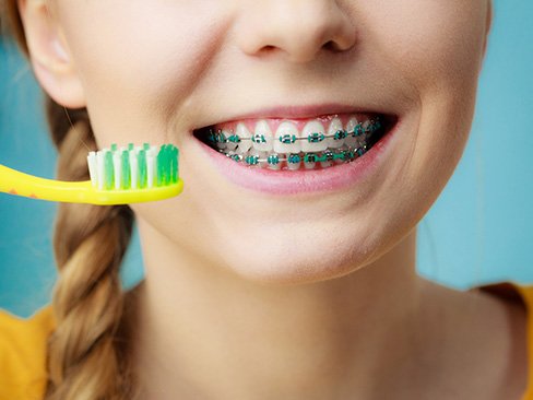 a teen with braces holding a toothbrush next to their mouth while smiling