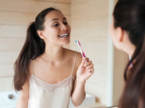 Woman brushing teeth after teeth whitening in Dallas