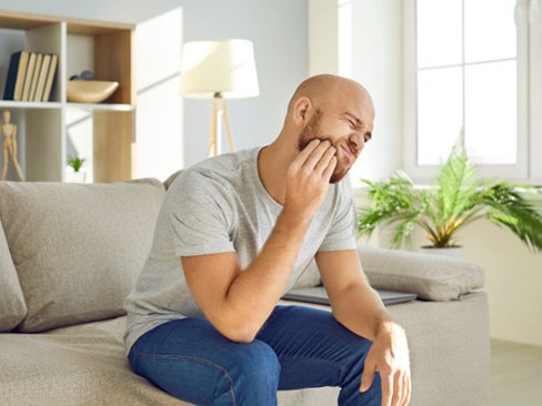 Man experiencing tooth pain on couch at home