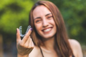 a woman smiling while holding her Invisalign aligner