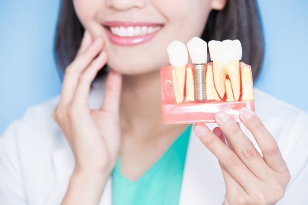 dentist smiling while holding dental implant model 