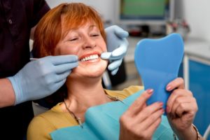 an older woman is happily looking at her new dental implants at the dentist’s office