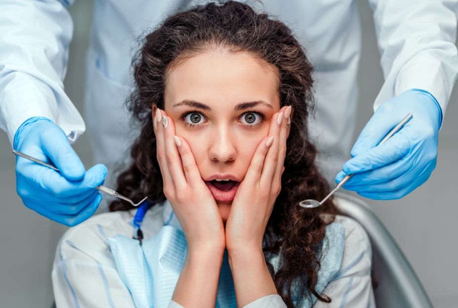 Woman in dental chair with hands on face, scared.